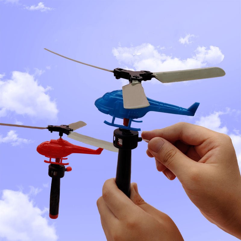 Hands holding pull-string launcher with blue and red helicopter toys flying against blue sky