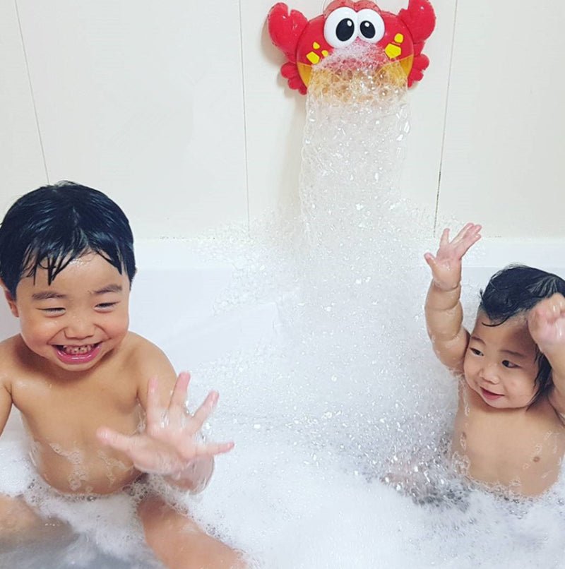 Two toddlers laughing in bubble-filled bathtub with red crab bubble blower mounted on wall