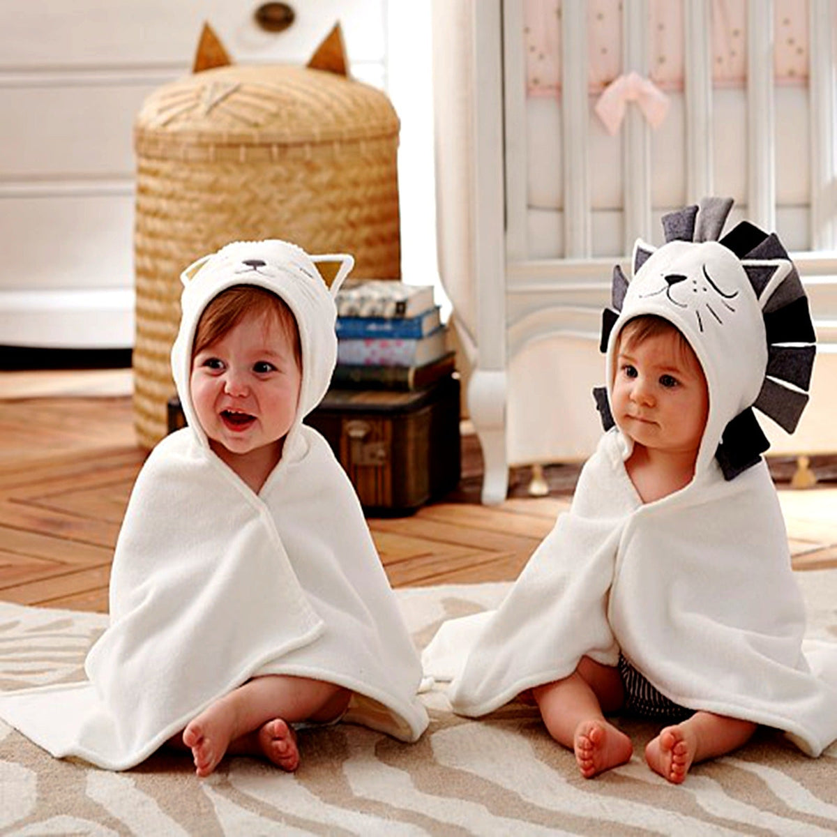 Two babies sitting wrapped in hooded bath towels showing cat style and lion style side by side