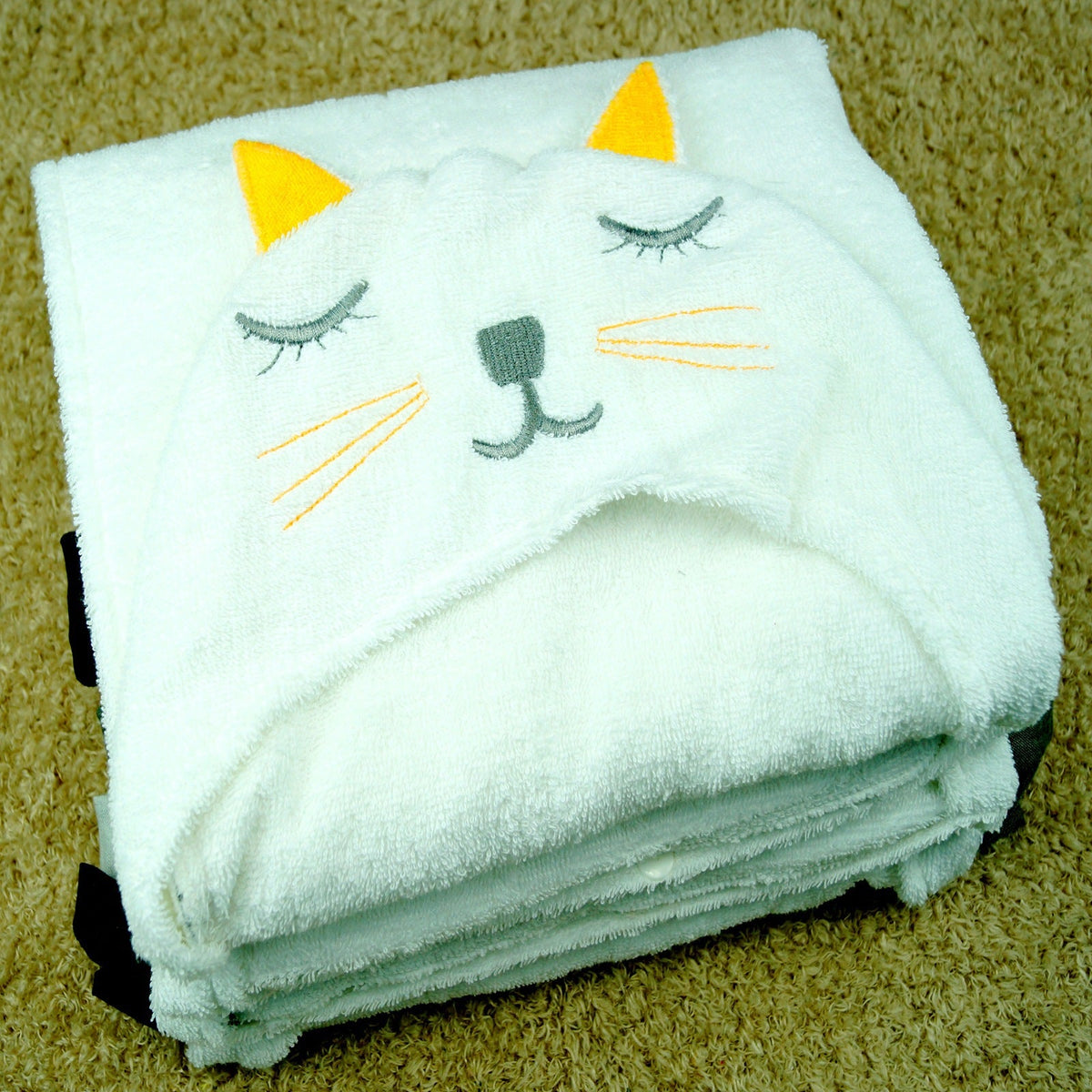 Folded cute cat hooded baby bath towel with yellow ears and embroidered face on carpet