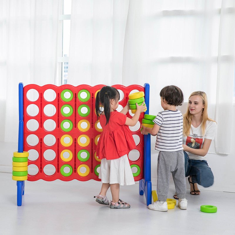 Two kids and mom playing giant connect four game indoors with green and yellow rings